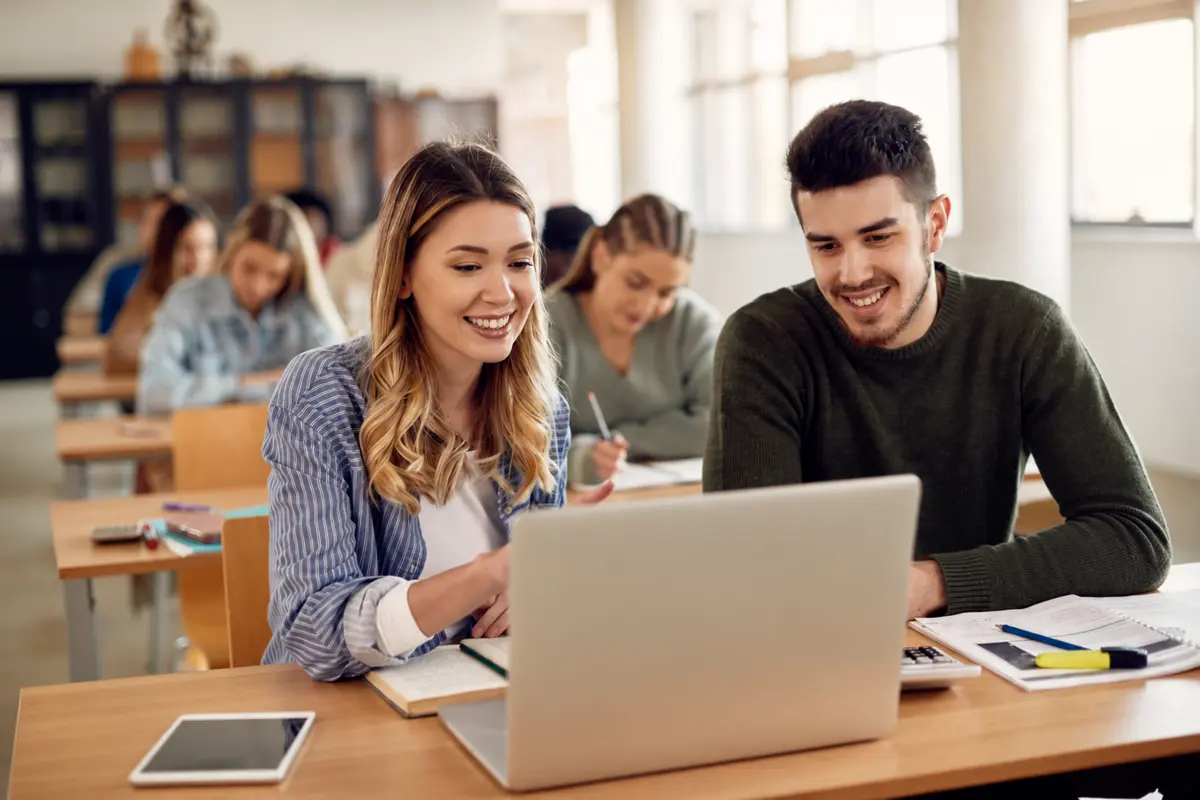 Two college students learning together using a laptop in a classroom
